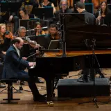 Un pianiste joue un morceau au tempo larghetto, entouré par un orchestre symphonique.