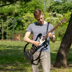 Un homme joue d'une guitare électrique sans ampli dans un parc verdoyant, profitant du beau temps pour faire de la musique en plein air.
