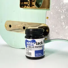 Flacon de "nitorlack relic patina" à côté d'une guitare électrique couleur menthe, prête pour un relicage guitare.