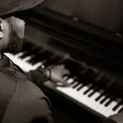 Un pianiste concentré joue un accord au piano, sa main effleurant les touches.