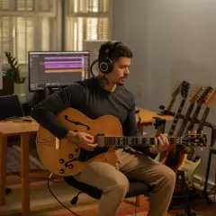 Un musicien concentré, casque sur les oreilles, joue d'une guitare acoustique dans un studio d'enregistrement. Il est prêt à enregistrer sa guitare acoustique.