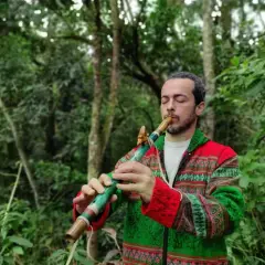 Un homme joue d'un instrument de musique à bec coloré dans une forêt luxuriante.