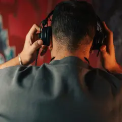 Un homme ajuste un type de casque audio sur ses oreilles, le dos tourné, devant un mur couvert de graffitis colorés.