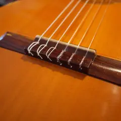 Gros plan sur le chevalet d'une guitare classique, où chaque corde est solidement attachée par un nœud corde guitare classique.