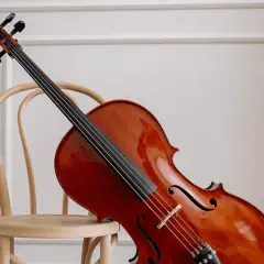 Un magnifique violoncelle en bois verni repose sur une chaise en bois clair, prêt à faire vibrer ses cordes.