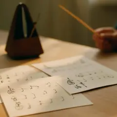 Partition de musique sur une table, avec un métronome et une baguette. Le rythme ternaire est palpable.