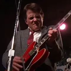 Marty McFly joue de sa guitare rouge emblématique sur scène, prêt à faire vibrer le public.