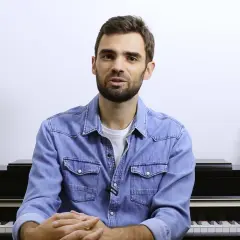 Un homme devant un piano, prêt à jouer. Ses mains sont croisées, attendant le moment de créer de la musique à quatre mains.