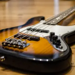 Gros plan sur une basse électrique sunburst posée sur un parquet en bois. Les cordes et les micros sont bien visibles.