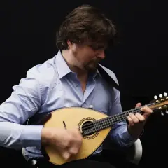 Un homme joue de la mandoline, son visage concentré sur l'instrument. Le son mélodieux de la mandoline emplit la pièce.