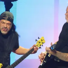 Robert Trujillo, bassiste de Metallica, joue avec passion sur scène, son instrument jaune vif contrastant avec le fond bleu.