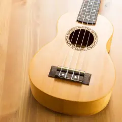 Un joli ukulélé en bois clair, prêt à jouer de la musique sur une table en bois.