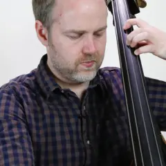 Un musicien joue un arpege basse, ses doigts glissant sur les cordes de la contrebasse.