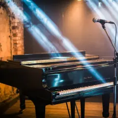 Un piano à queue noir, prêt pour un concert, sous des rayons de lumière bleus et dorés. Le micro est en place, attendant la première note de si bémol piano.