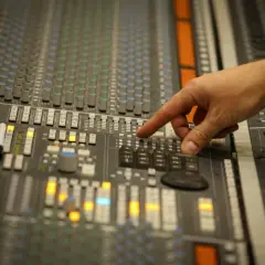 Main d'un ingénieur du son ajustant les faders d'une console de mixage pour un sound check.