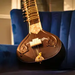 Un magnifique sitar indien repose sur un fauteuil bleu profond, prêt à faire vibrer ses cordes.
