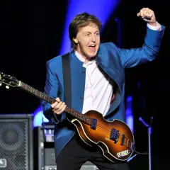 Paul McCartney, icône du rock, joue de sa basse Höfner sur scène, poing levé dans un geste d'enthousiasme.