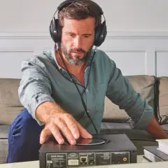 Homme concentré, casque audio sur les oreilles, ajustant un appareil. Il semble tester l'impédance de son casque audio pour une écoute parfaite.