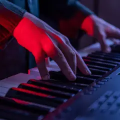Mains éclairées par la lumière rouge jouant sur les touches d'un piano, créant une ambiance musicale.