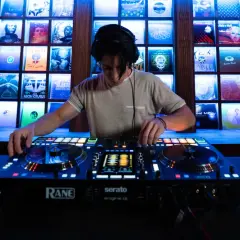 Un DJ mixe sur une console Rane, avec des vinyles rétro éclairés en fond. Fiche technique DJ.