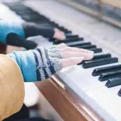 Les doigts de pianiste, vêtus de mitaines colorées, effleurent les touches d'un piano, créant une mélodie douce.