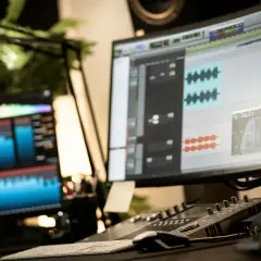 Post-production audio, avec des formes d'onde et des pistes sur écran. Un léger micro-bleed de lumière sur le côté gauche.