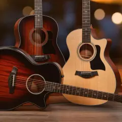 Trois guitares acoustiques, dont une en palissandre, posées sur un parquet en bois. L'arrière-plan est flou et lumineux.