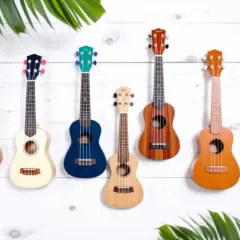 Sept ukulélés de différentes couleurs et tailles, dont un ukulélé de taille soprano, sont accrochés sur un mur en bois blanc, entourés de feuilles vertes.