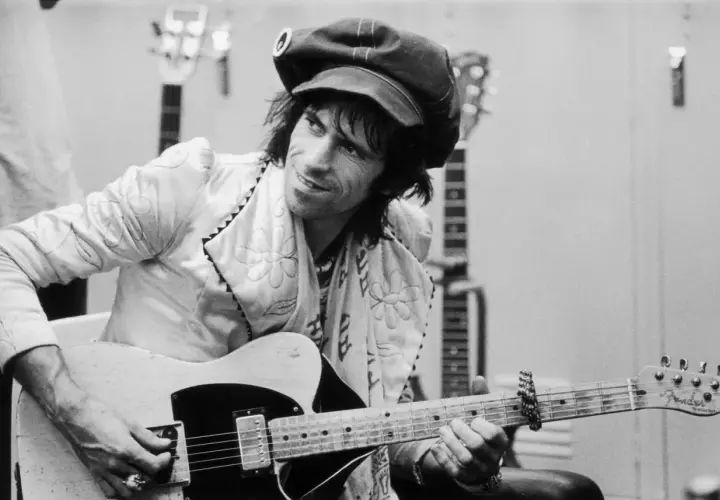 Keith Richards, casquette sur la tête, joue de sa guitare Fender Telecaster, entouré d'autres guitares.