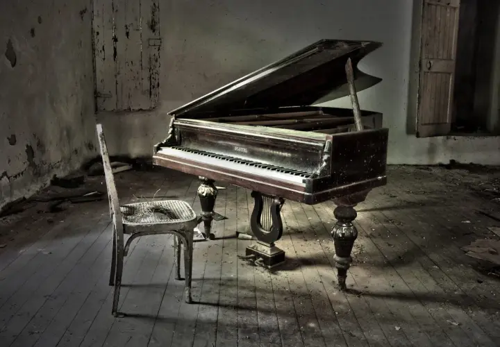 Un piano à queue poussiéreux dans une pièce abandonnée, avec une chaise usée. La hauteur du tabouret du piano semble parfaite pour jouer.