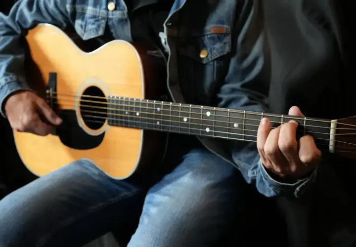 Un guitariste en jean montre comment tenir une guitare, ses doigts formant un accord sur le manche.