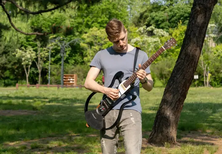 Un homme joue d'une guitare électrique sans ampli dans un parc verdoyant, profitant du beau temps pour faire de la musique en plein air.