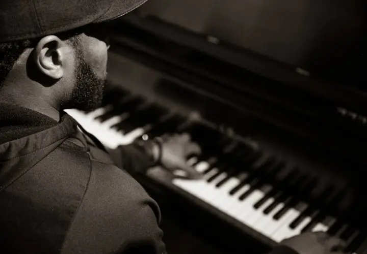 Un pianiste concentré joue un accord au piano, sa main effleurant les touches.