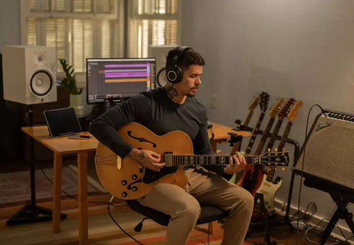 Un musicien concentré, casque sur les oreilles, joue d'une guitare acoustique dans un studio d'enregistrement. Il est prêt à enregistrer sa guitare acoustique.
