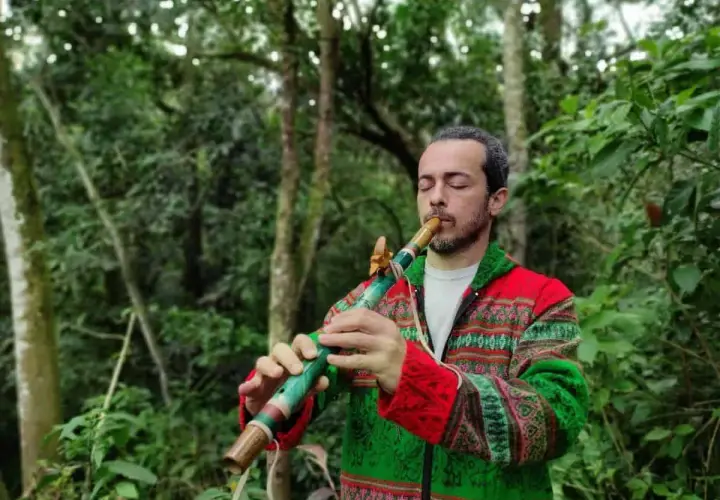 Un homme joue d'un instrument de musique à bec coloré dans une forêt luxuriante.