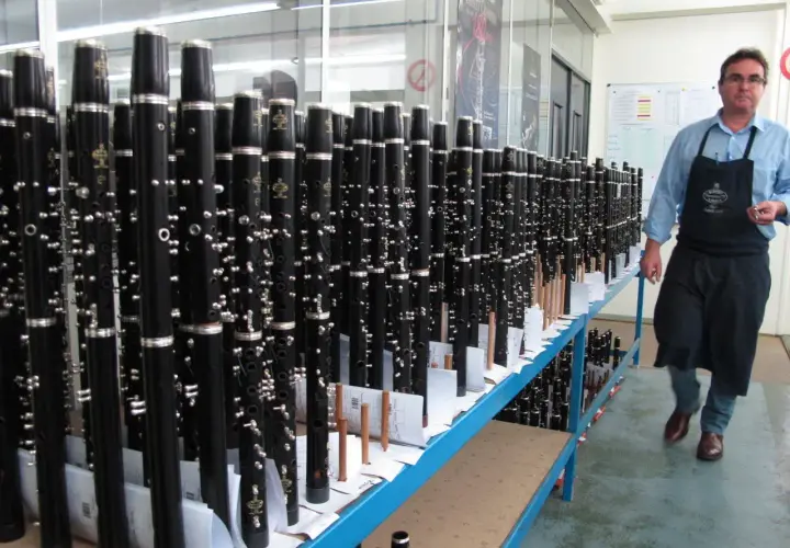 Un homme en tablier inspecte un buffet de clarinettes, prêt à être expédié. Ces instruments de musique, des modèles "crampon mantes", sont alignés sur des étagères.