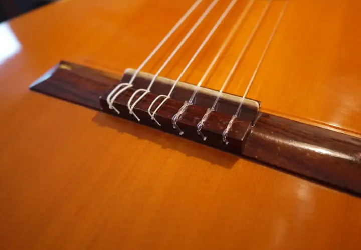 Gros plan sur le chevalet d'une guitare classique, où chaque corde est solidement attachée par un nœud corde guitare classique.