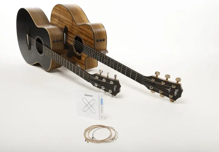 Deux guitares acoustiques, une noire et une en bois naturel, prêtes à produire le son de la guitare. Un jeu de cordes D'Addario est posé devant.