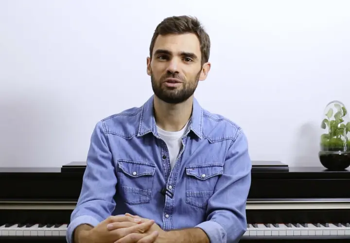 Un homme devant un piano, prêt à jouer. Ses mains sont croisées, attendant le moment de créer de la musique à quatre mains.