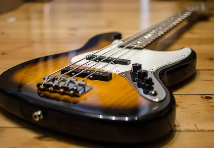 Gros plan sur une basse électrique sunburst posée sur un parquet en bois. Les cordes et les micros sont bien visibles.