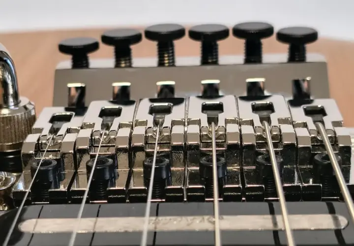 Gros plan sur le chevalet d'une guitare électrique, avec le bras de trémolo visible. Les six pontets chromés sont alignés, prêts à produire des notes vibrantes grâce au système de tremolo.