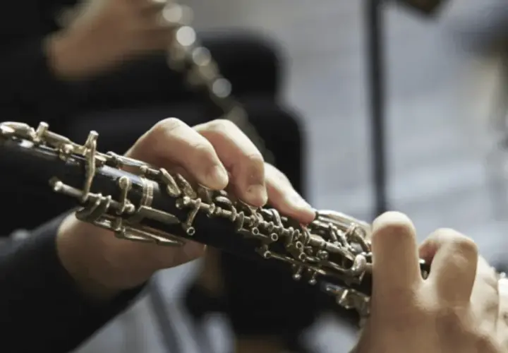 Mains jouant d'un hautbois, un instrument à vent aux clés complexes, évoquant la musique classique.