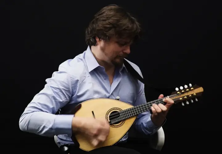 Un homme joue de la mandoline, son visage concentré sur l'instrument. Le son mélodieux de la mandoline emplit la pièce.