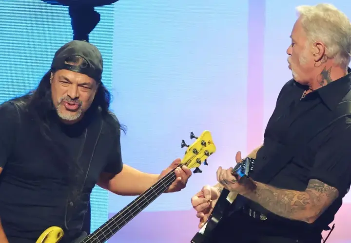 Robert Trujillo, bassiste de Metallica, joue avec passion sur scène, son instrument jaune vif contrastant avec le fond bleu.