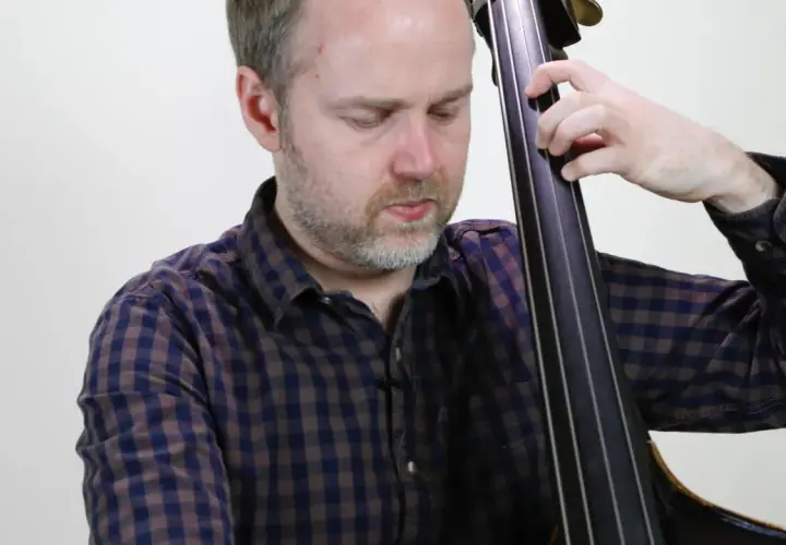 Un musicien joue un arpege basse, ses doigts glissant sur les cordes de la contrebasse.