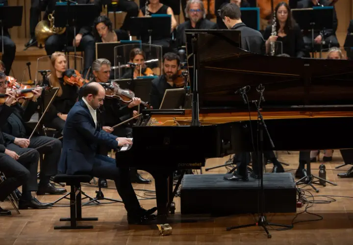 Un pianiste joue un morceau au tempo larghetto, entouré par un orchestre symphonique.
