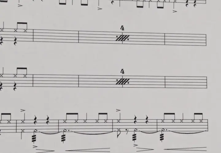 Partitions musicales avec des notes de batterie et des indications de tempo. Le symbole de répétition musique est présent, suggérant une section à rejouer.