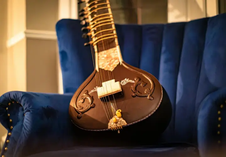 Un magnifique sitar indien repose sur un fauteuil bleu profond, prêt à faire vibrer ses cordes.