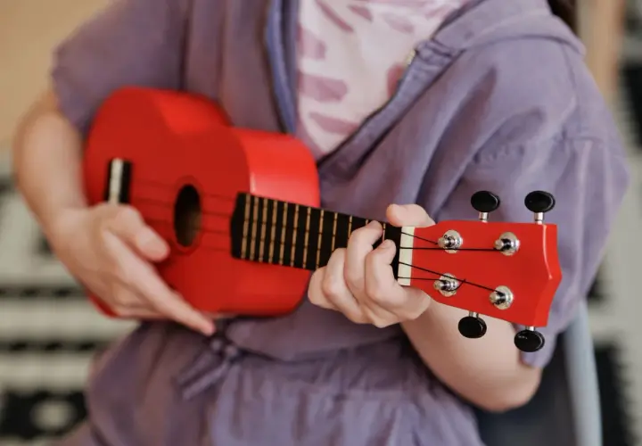 Enfant jouant d'un petit instrument de musique rouge vif, un ukulélé, avec concentration.