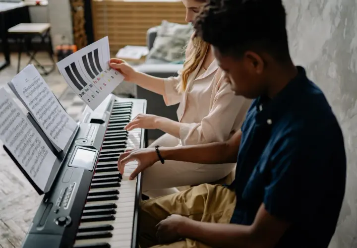 Deux mains jouent sur un piano, l'une suit une partition, l'autre une feuille avec des notes comme sol#m.